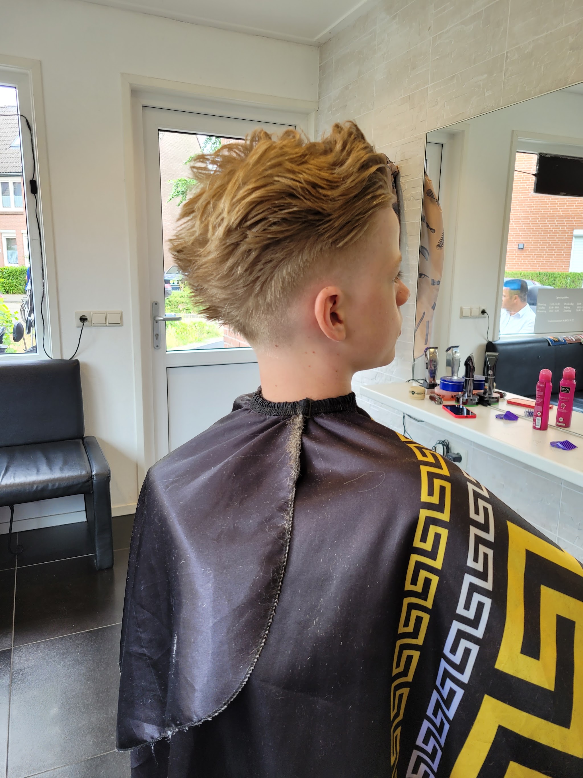 Blond haar met textuur bovenop en kort opzij, van achteren, met de spiegel en de toonbank van de zaak